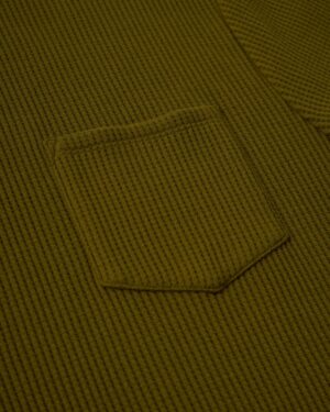 Close-up of The Cannes Waffle Knit Tee in Arbequina by Dandy Del Mar, showcasing its green waffle-knit fabric and small sewn pocket.