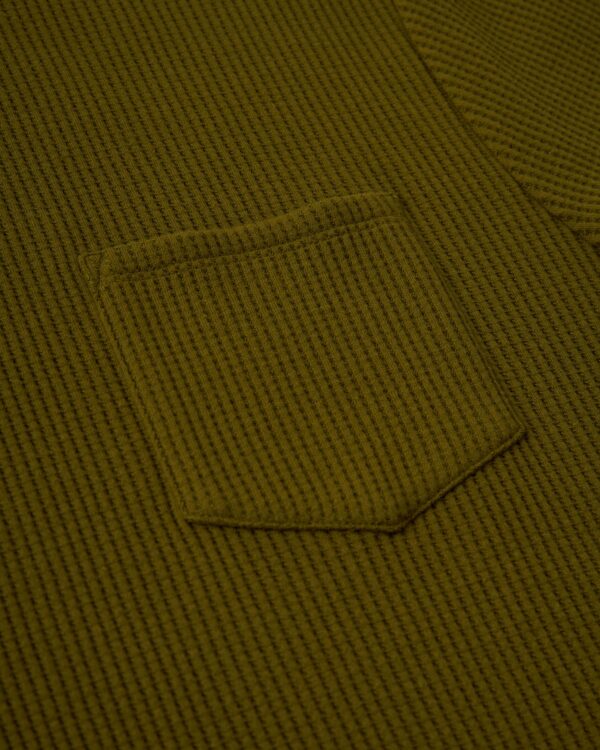 Close-up of The Cannes Waffle Knit Tee in Arbequina by Dandy Del Mar, showcasing its green waffle-knit fabric and small sewn pocket.