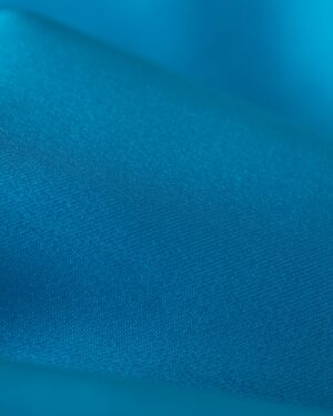Close-up of the elegant Catania Satin Angel Sleeve Dress by Dandy Del Mar in Lago, showcasing its smooth, subtle texture.
