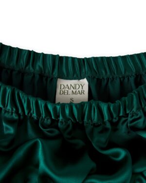 Close-up of a dark green satin garment with an elastic waistband, displaying a label reading 