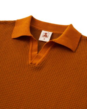 The Sebastian Long Sleeve Polo in Burnt Sienna by Dandy Del Mar features a V-neck, collar, and long sleeves. Crafted from 100% cotton for comfort, it includes a small inner label with the logo and size 