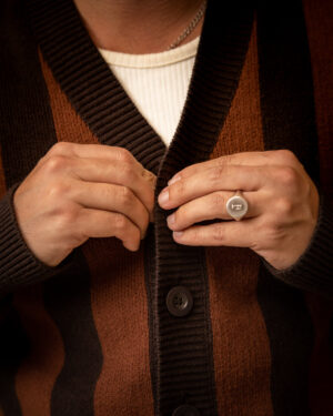 A person buttoning The Florence Knit Cardigan - Garam by Dandy Del Mar, featuring a brown and black jacquard knit, wears a silver ring on the left hand.