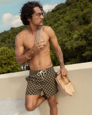 MAN IN SWIM SHORTS LEANING ON ROOFTOP WALL